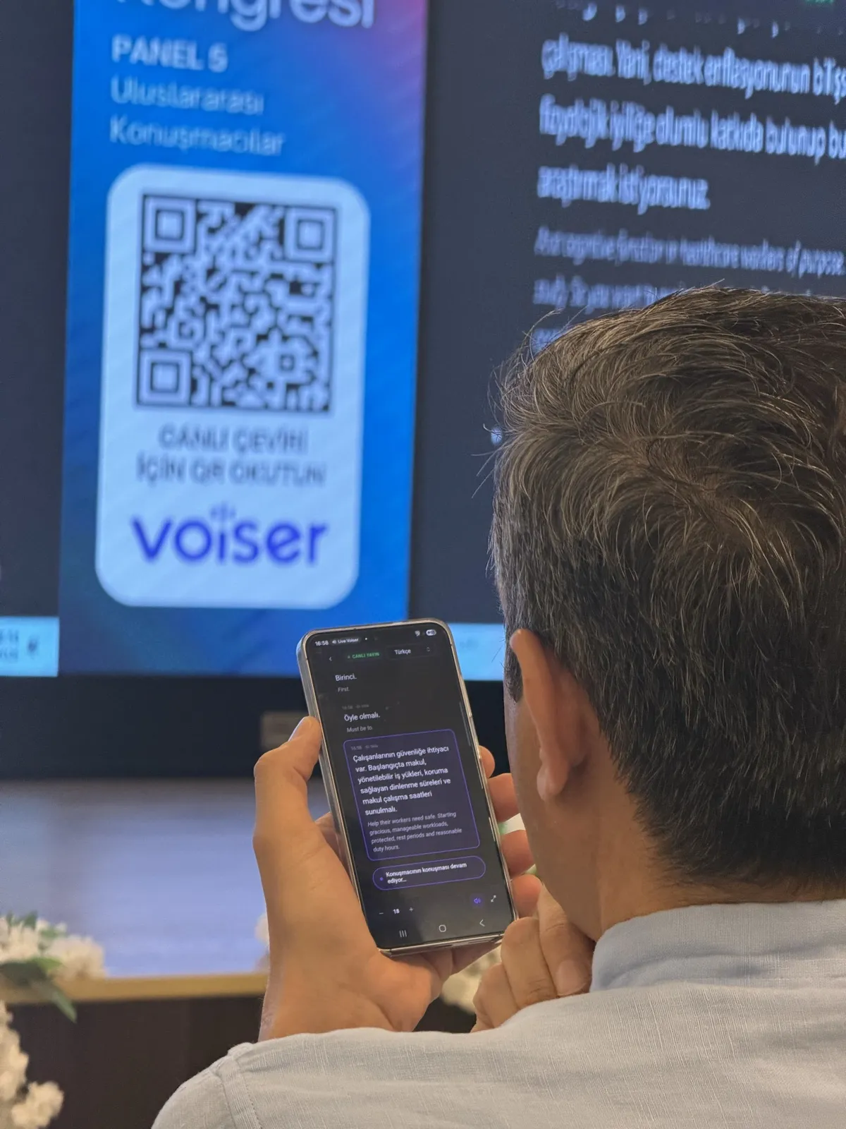 Salonda canlı çeviriyi telefonundan takip eden bir katılımcı
